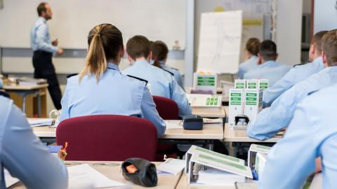 Polizeianwärterinnen und -anwärter sitzen uniformiert in einem Hörsaal. Ein...