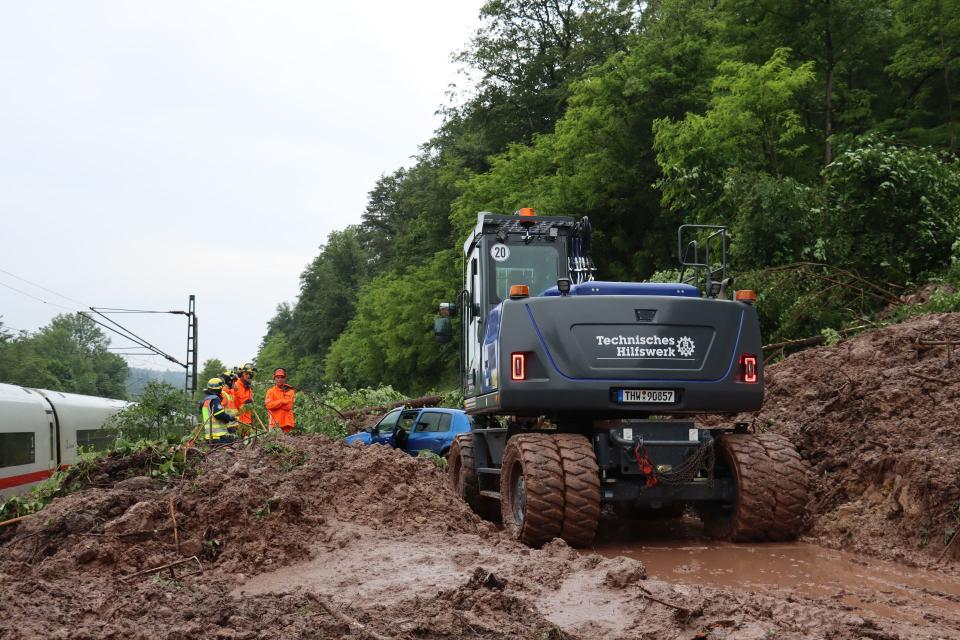 THW-Kräfte ziehen mit Hilfe eines Baggers ein Auto aus dem Schlamm